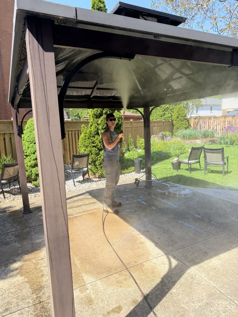 Pressure washing a stamped concrete patio, the cleaned strip showing bright against the surrounding surface.