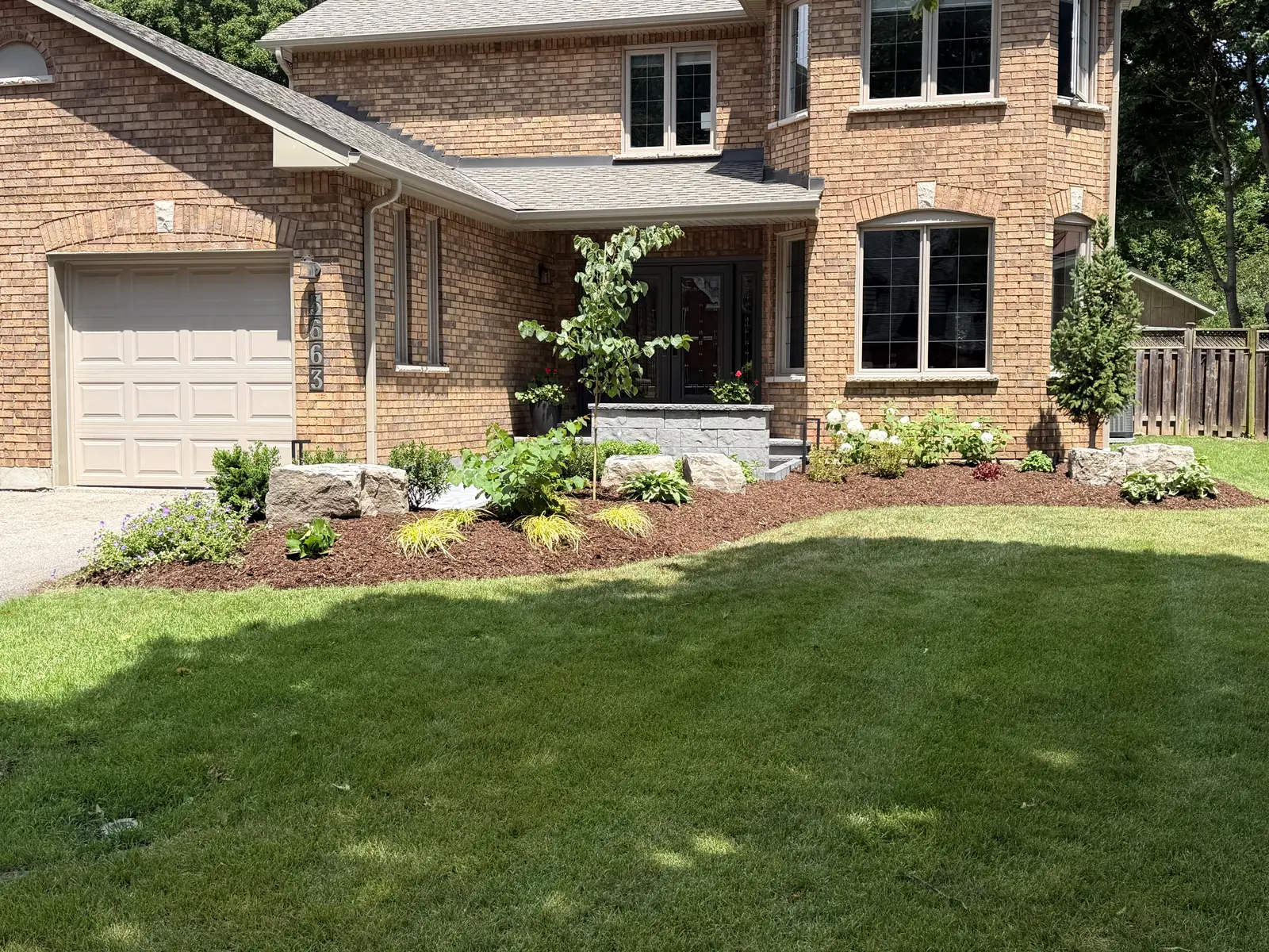 Finished front beds at a brick house — layered planting, boulders and a clean mulch edge.