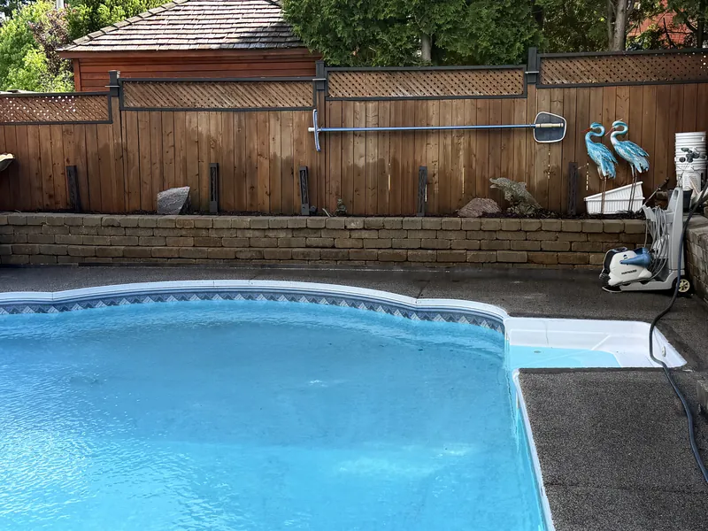Stacked stone retaining wall holding the grade along a poolside fence line.