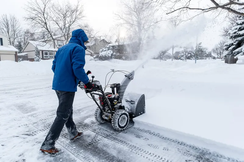 Two-stage snow blower clearing a residential driveway after a heavy fall.